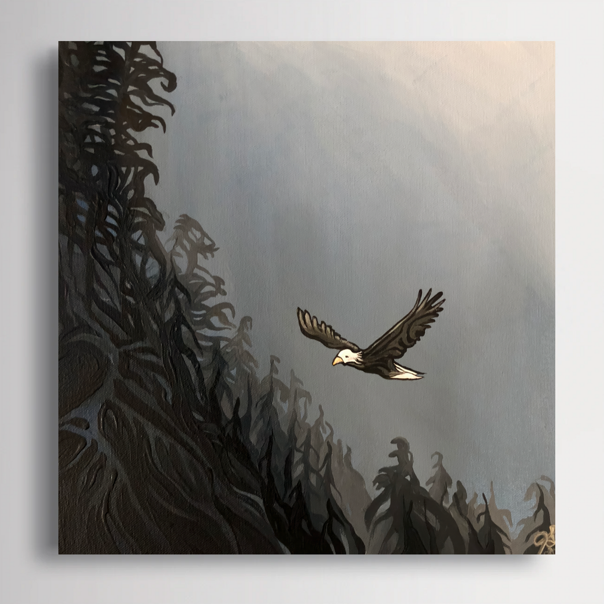 A square painting or canvas showing a bald eagle flying over dark, textured tree silhouettes against a pale misty sky, photographed hanging on a light gray wall.