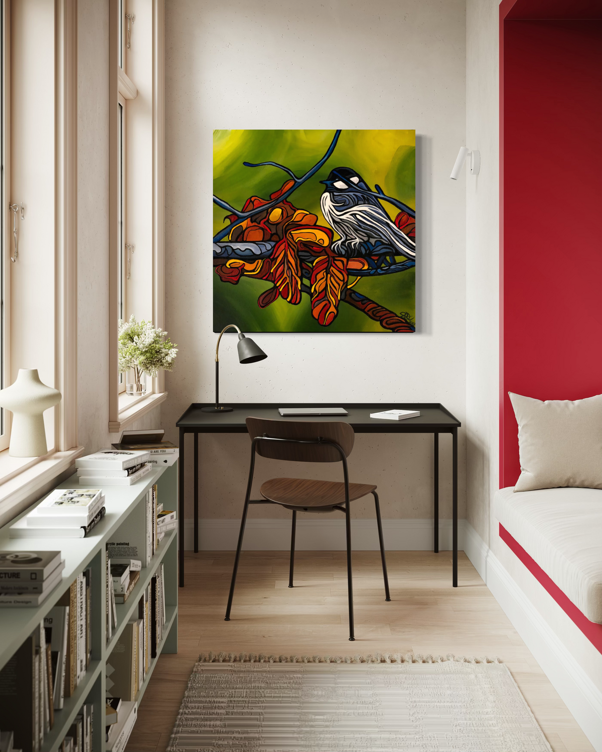 A colorful square wall art print Jeff Dillon FIne Art depicting a bird perched on branches with green, yellow, orange, and red tones, displayed above a black desk in a modern room with a red accent wall.