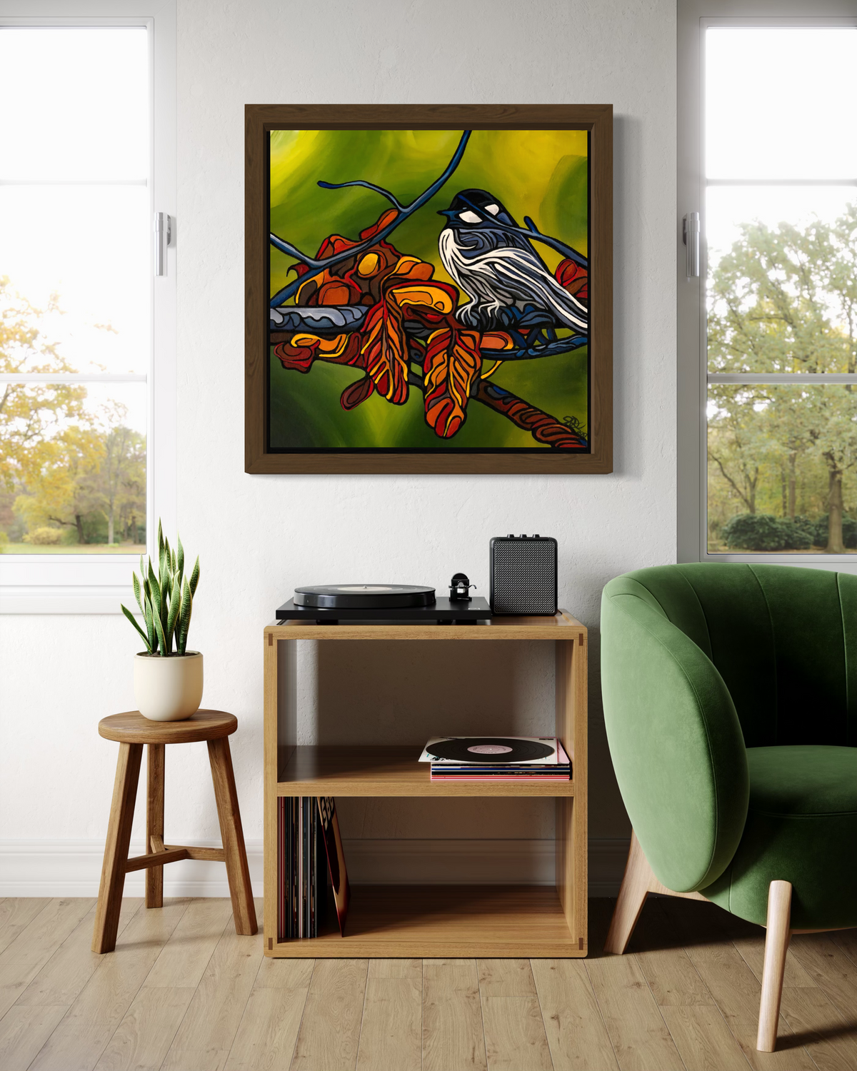 A framed square wall art print Jeff Dillon FIne Art depicting a bird perched on a branch with bright green, yellow, orange, and red tones, displayed above a wooden shelf in a styled room with a green chair, windows, and a plant.